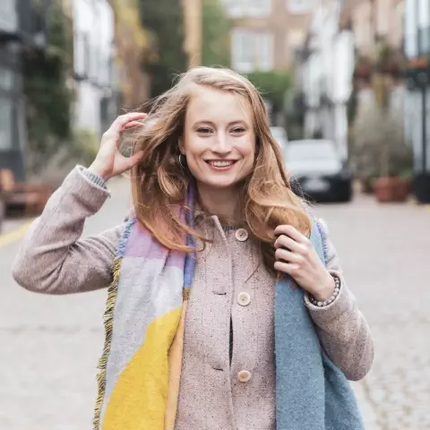 Picture of a woman wrapped in a multi-colored shawl touching her hair on a street in Portobello